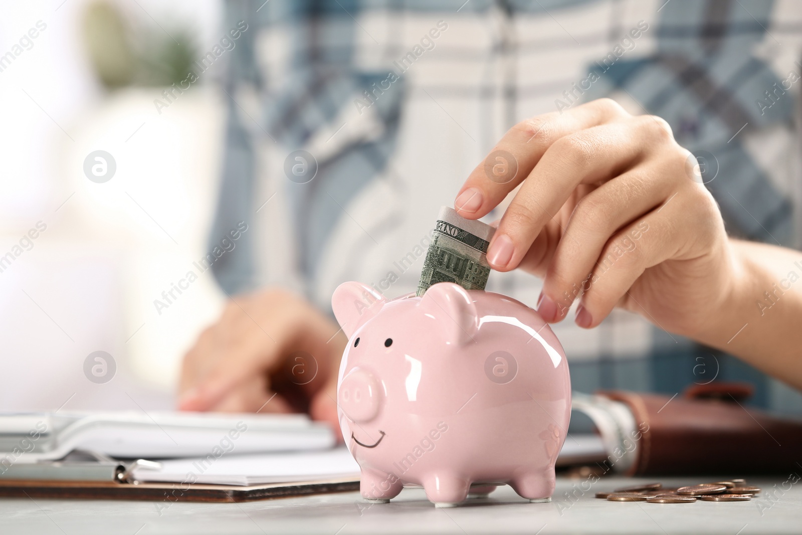 Photo of Woman putting money into piggy bank at table indoors, closeup