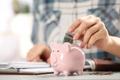 Photo of Woman putting money into piggy bank at table indoors, closeup