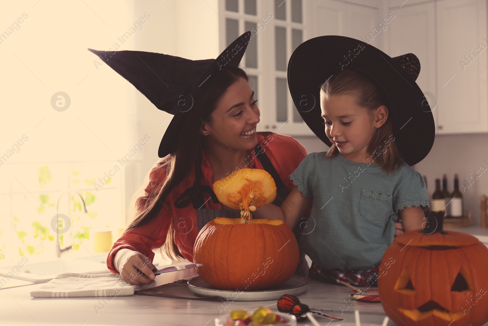 Photo of Mother and daughter making pumpkin jack o'lantern at table in kitchen. Halloween celebration