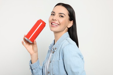 Beautiful happy woman holding red beverage can on light grey background