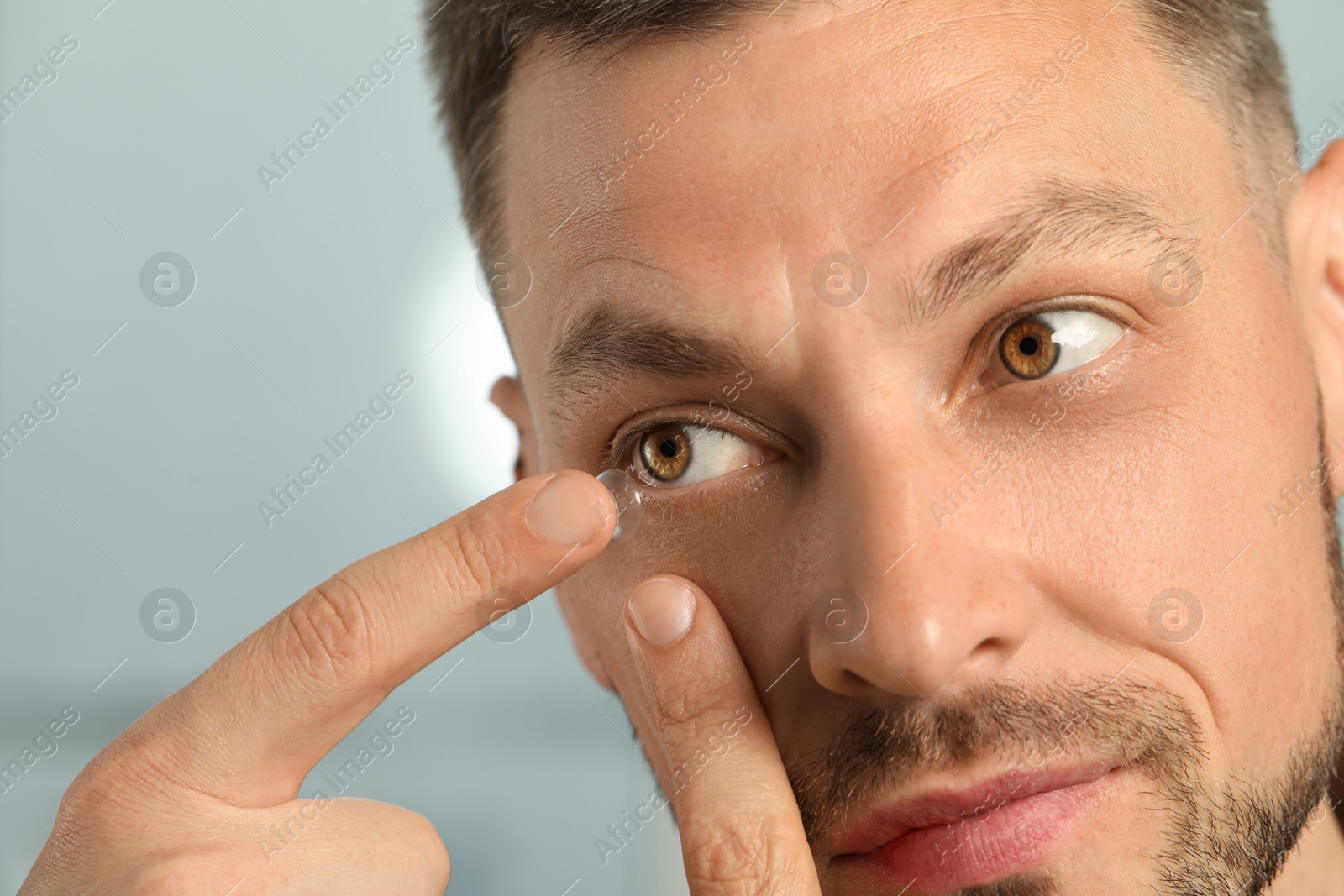 Photo of Man putting contact lens in his eye on blurred background, closeup