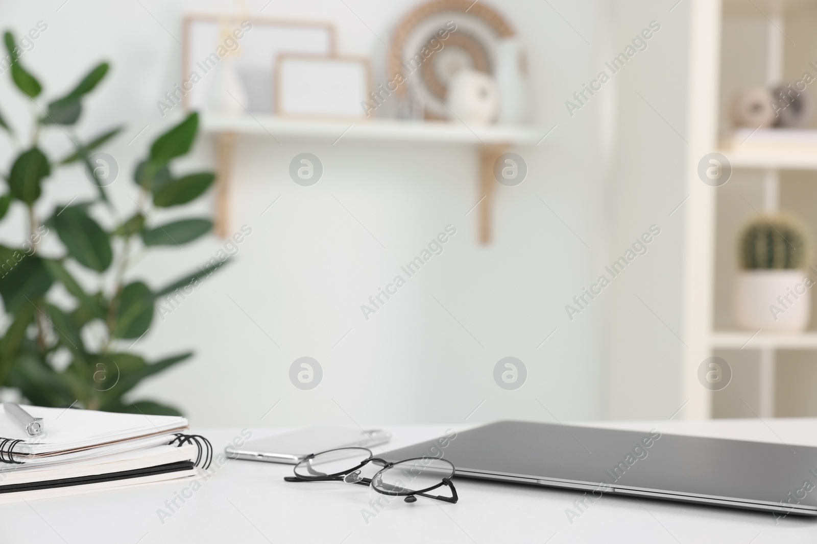 Photo of Home office. Laptop, glasses, notebooks, smartphone and pen on white desk indoors. Space for text