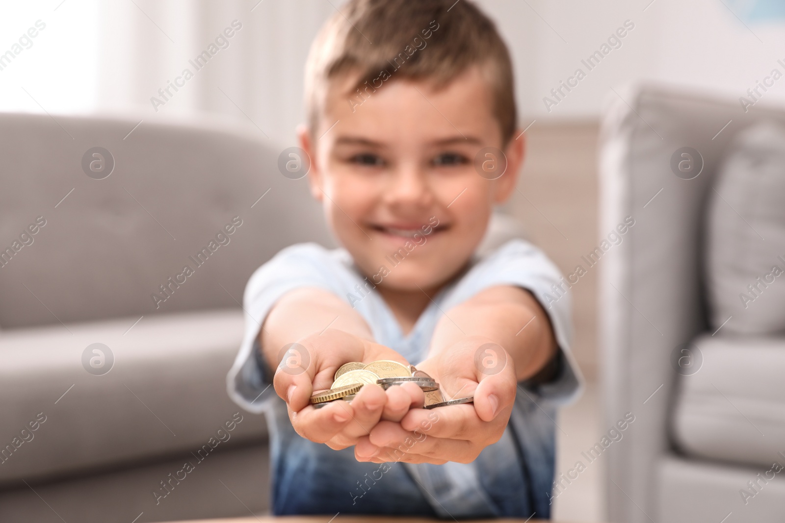 Photo of Happy cute little boy holding coins at home, focus on hands