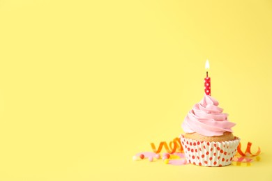 Photo of Delicious birthday cupcake with burning candle, sprinkles and streamer on yellow background, space for text