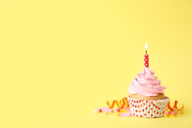 Delicious birthday cupcake with burning candle, sprinkles and streamer on yellow background, space for text