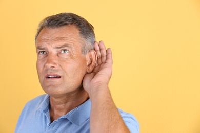 Photo of Mature man with hearing problem on color background. Space for text