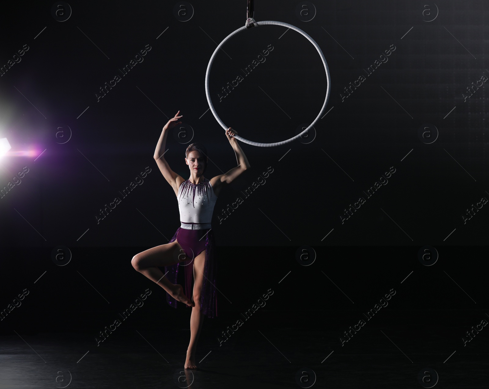 Photo of Young woman performing acrobatic element on aerial ring indoors. Space for text
