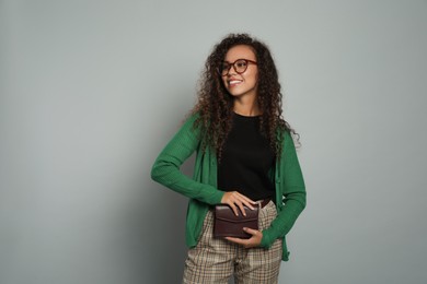 Beautiful African American woman with stylish waist bag on grey background