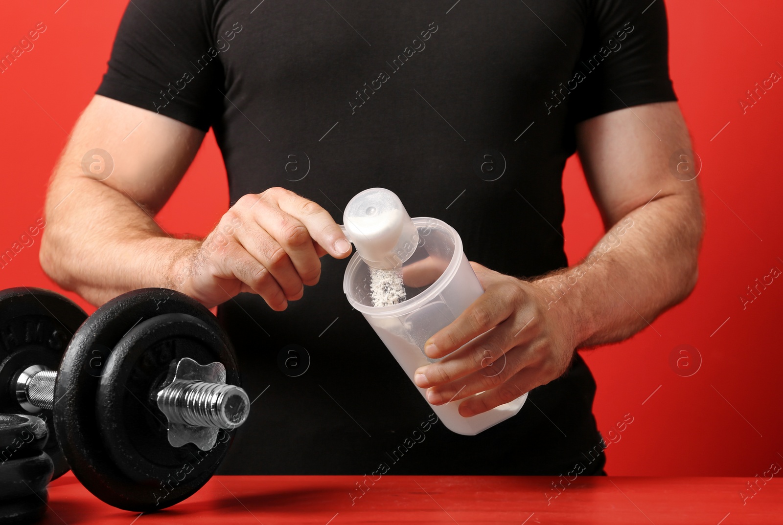 Photo of Man preparing protein shake at wooden table against red background, closeup