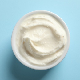 Bowl of tasty cream cheese on color background, top view