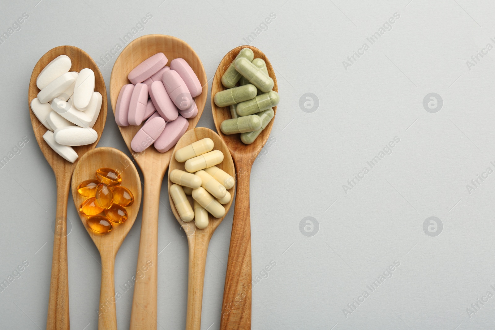 Photo of Different vitamin pills in spoons on light grey background, flat lay and space for text. Health supplement