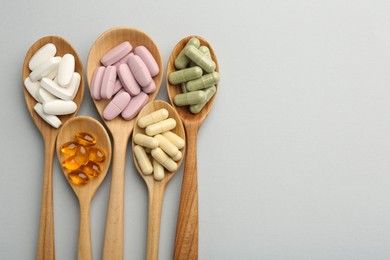 Different vitamin pills in spoons on light grey background, flat lay and space for text. Health supplement