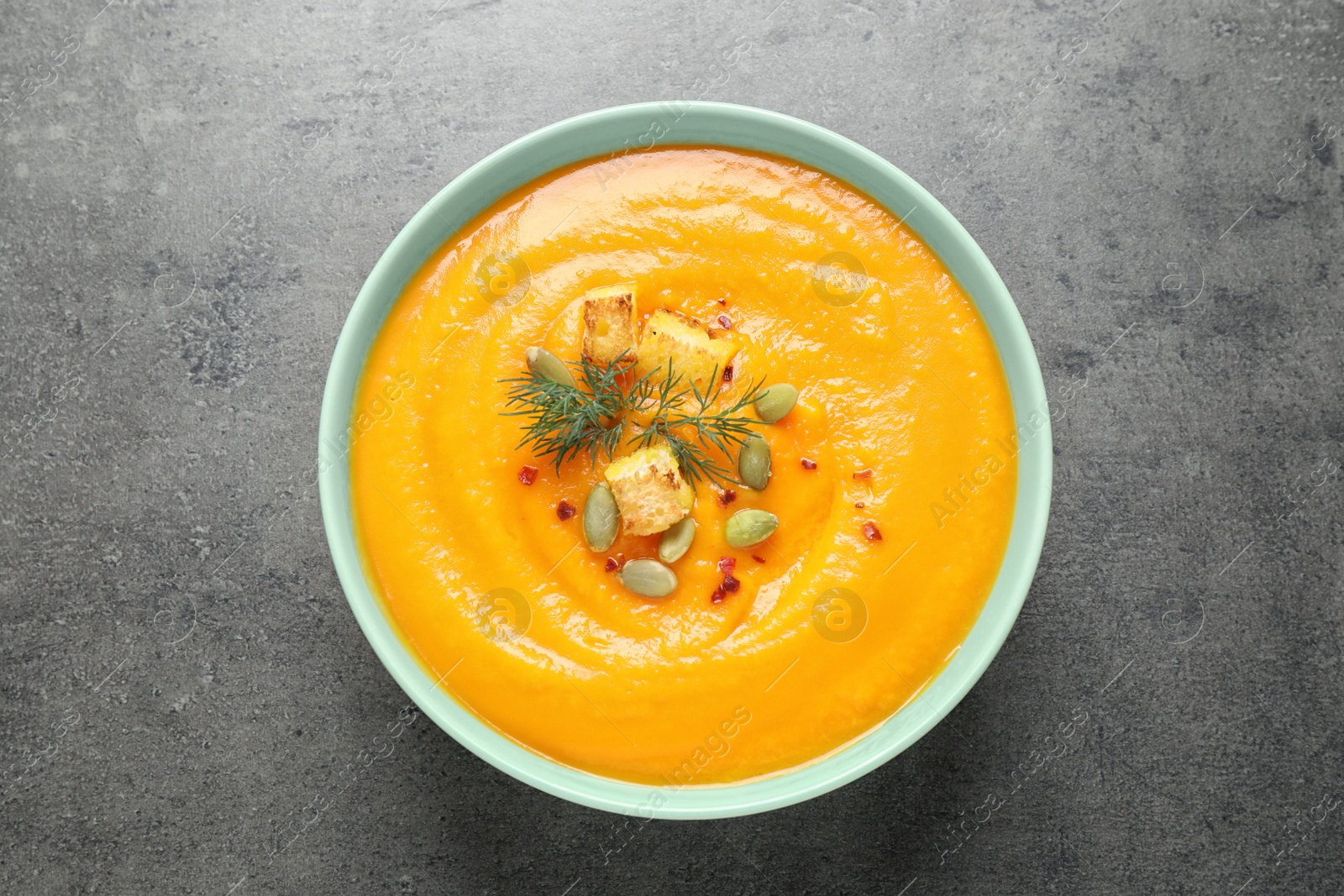 Photo of Delicious pumpkin soup in bowl on grey table, top view