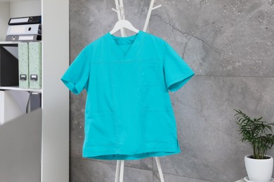 Photo of Turquoise medical uniform hanging on rack in clinic