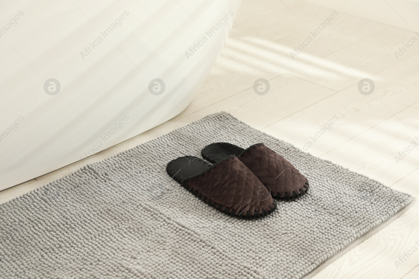 Photo of New grey bath mat with soft slippers near tub indoors