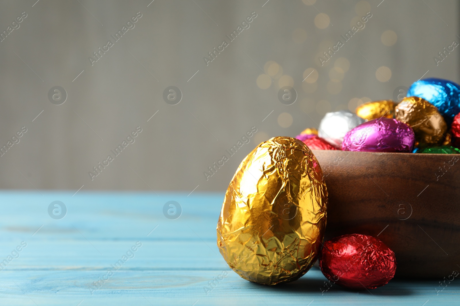 Photo of Chocolate eggs wrapped in colorful foil on light blue wooden table. Space for text