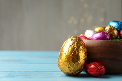 Photo of Chocolate eggs wrapped in colorful foil on light blue wooden table. Space for text