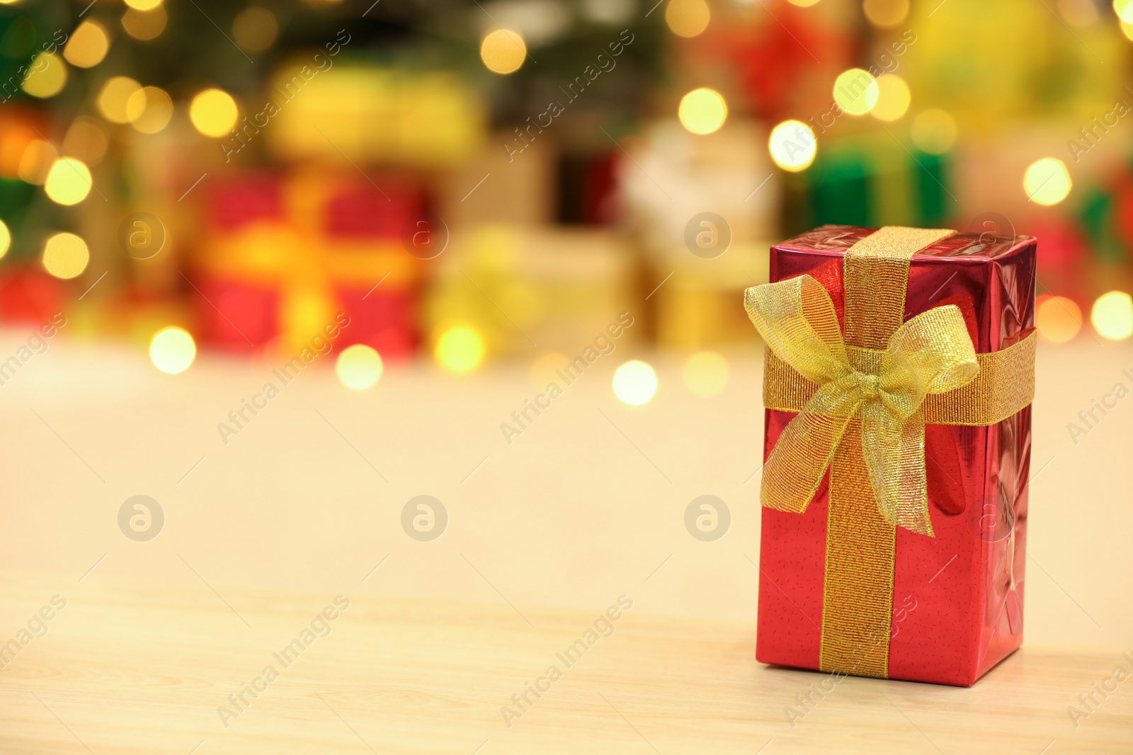 Photo of Beautifully wrapped gift box on wooden table against blurred festive lights, space for text. Christmas celebration