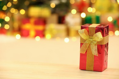 Photo of Beautifully wrapped gift box on wooden table against blurred festive lights, space for text. Christmas celebration