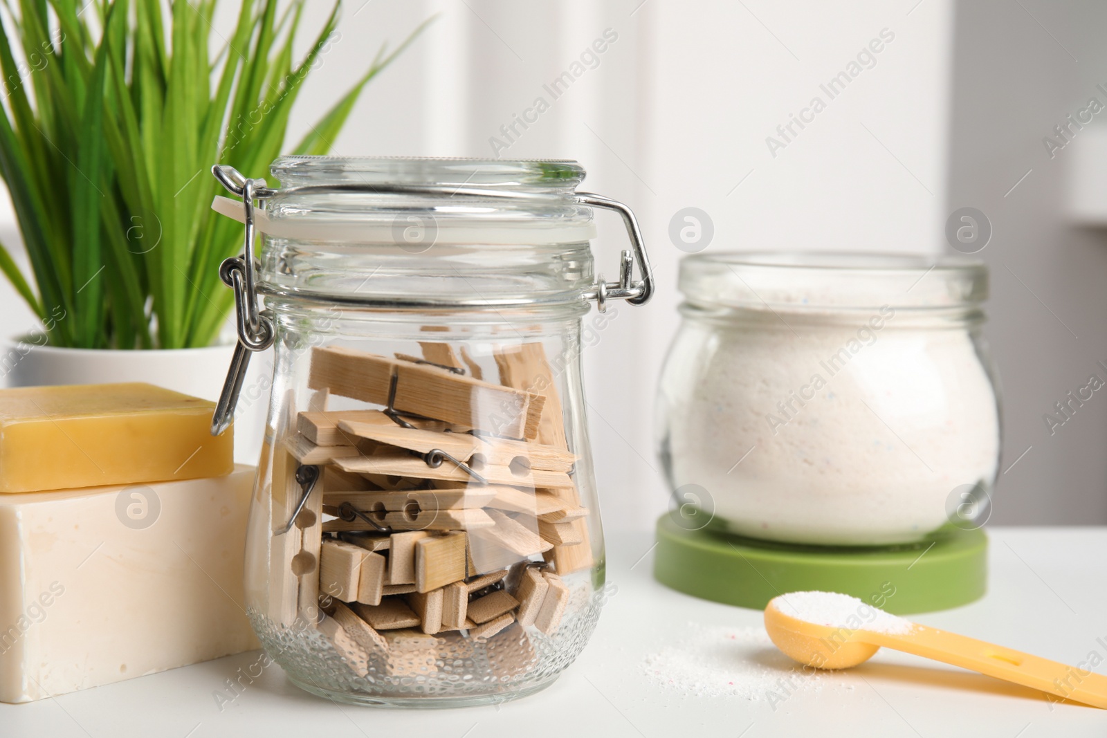 Photo of Many wooden clothespins in glass jar near soap bars and laundry powder on white table