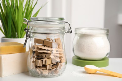 Many wooden clothespins in glass jar near soap bars and laundry powder on white table