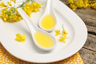 Photo of Rapeseed oil in gravy boats and beautiful yellow flowers on wooden table, closeup