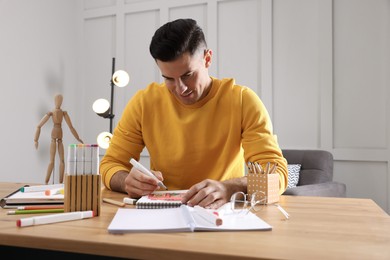 Photo of Man drawing in sketchbook with felt tip pen at wooden table indoors