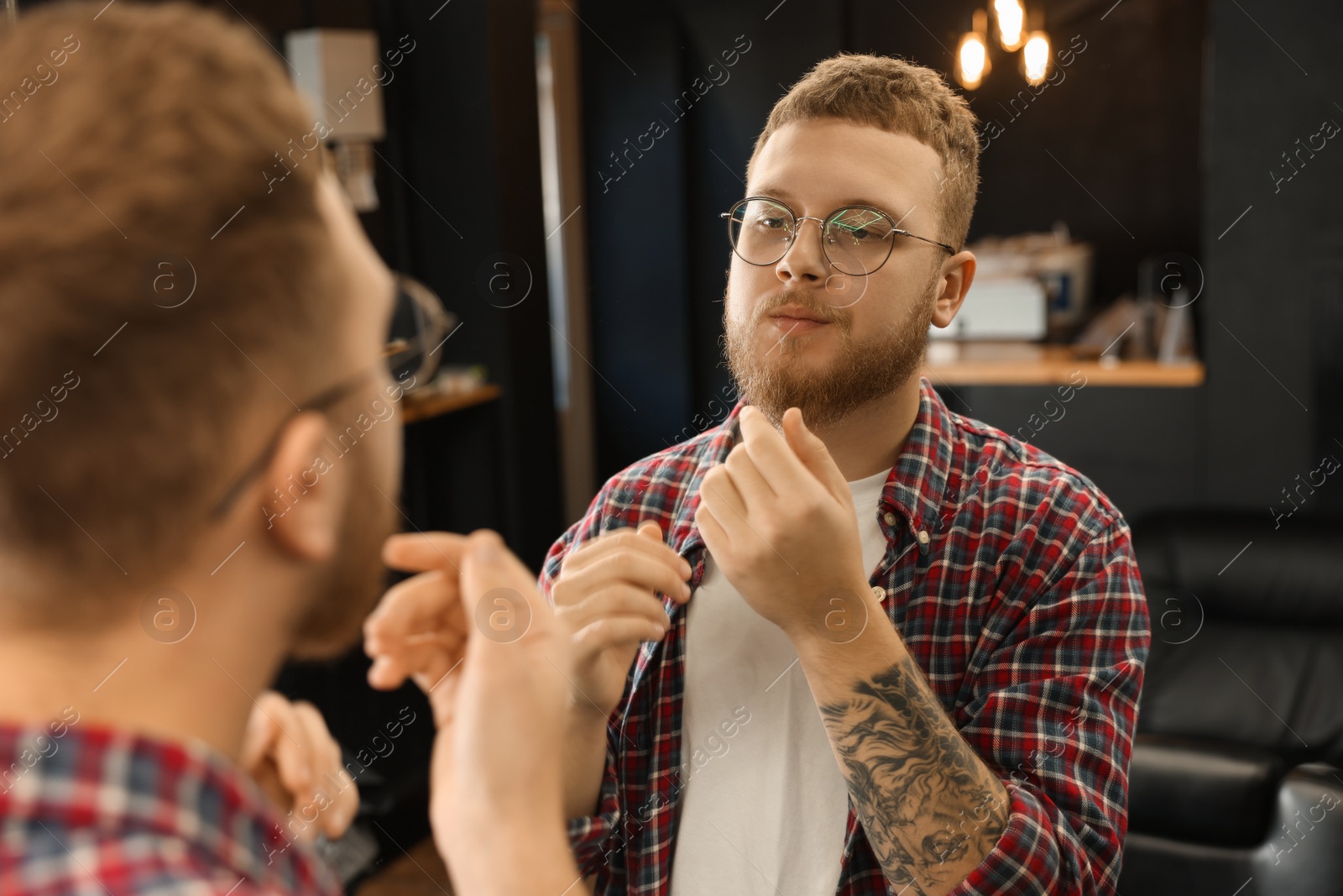 Photo of Young bearded man near mirror in barbershop