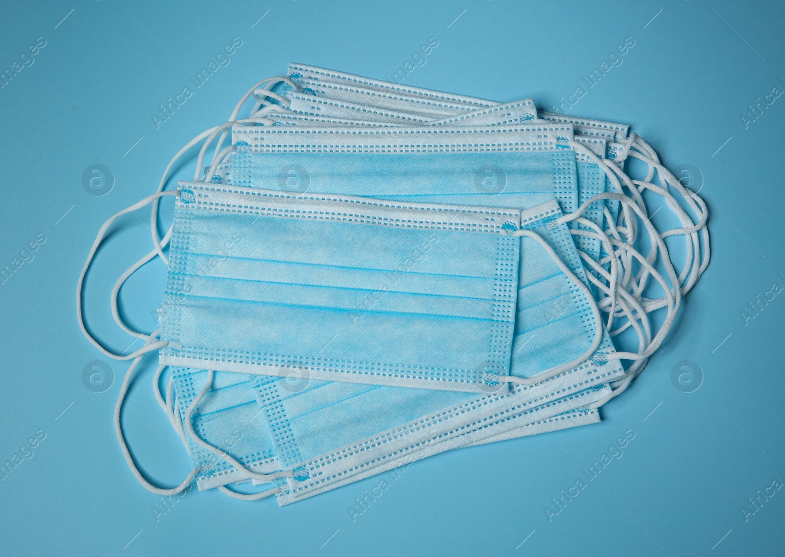 Photo of Disposable face masks on light blue background, flat lay. Protective measures during coronavirus quarantine