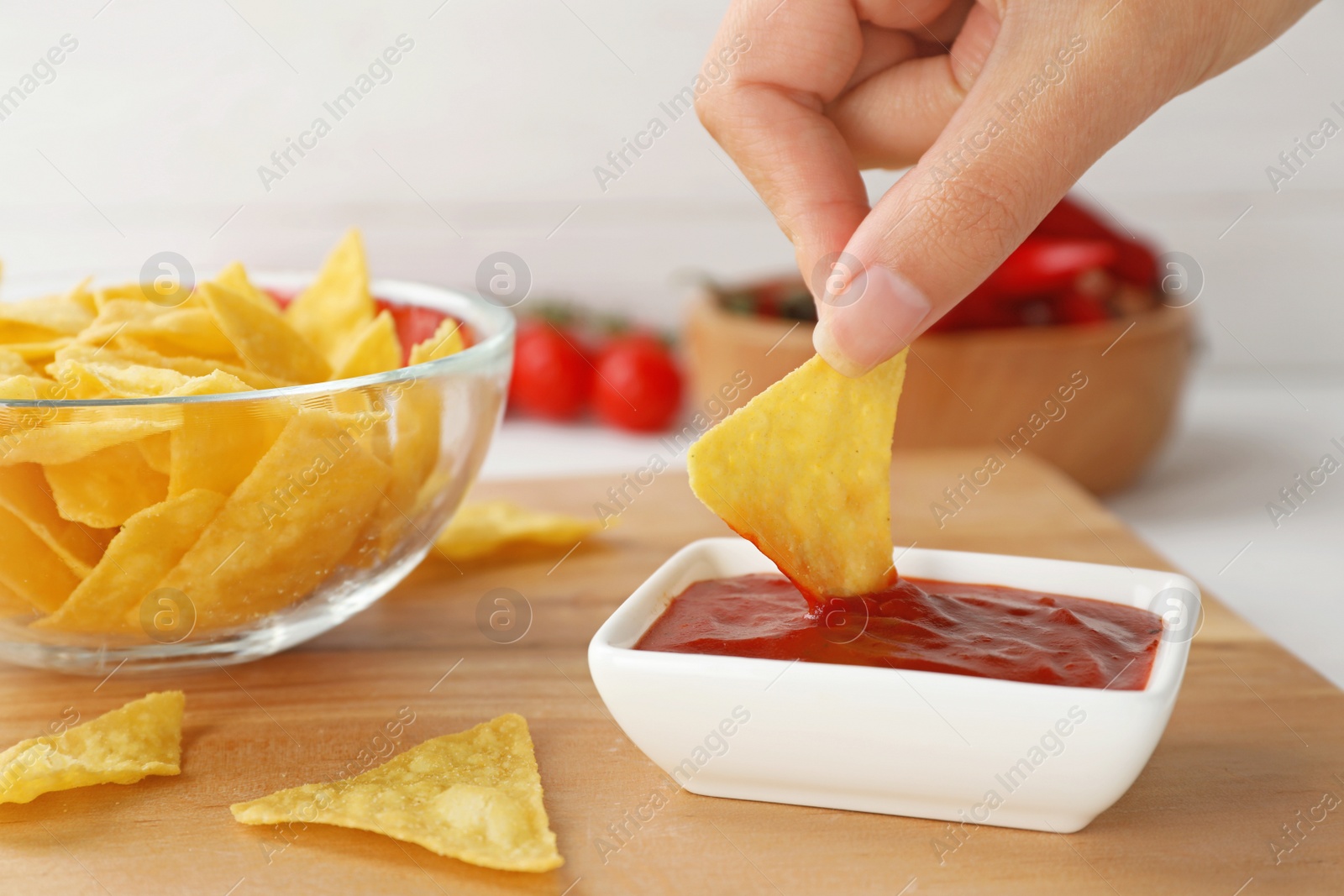 Photo of Woman dipping chip into hot chili sauce in bowl on table