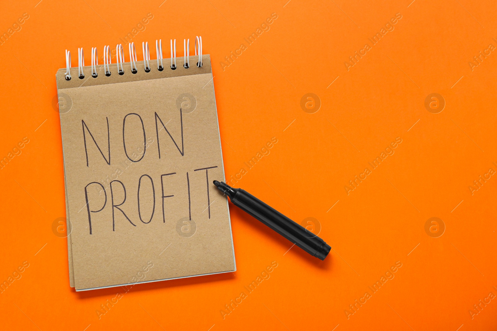 Photo of Notebook with phrase Non Profit and pen on orange background, flat lay. Space for text