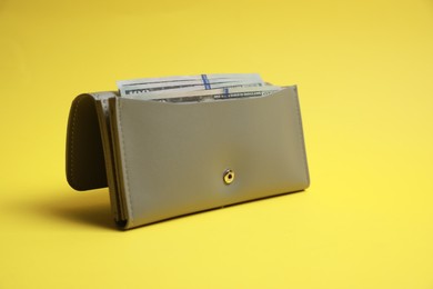 Photo of Stylish light grey leather purse with dollar banknotes on yellow background