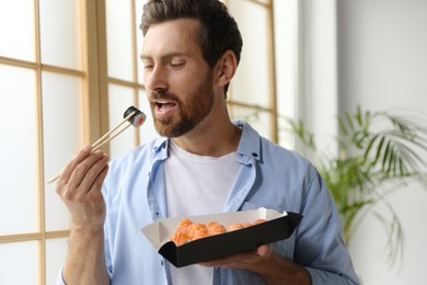 Photo of Handsome man eating sushi rolls with chopsticks indoors