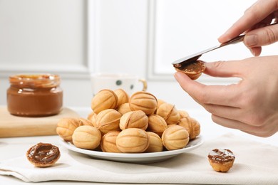 Photo of Woman spreading boiled condensed milk onto walnut shaped cookie indoors, closeup