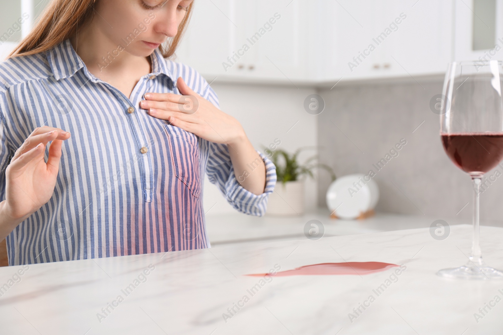 Photo of Woman with wine stain on her shirt at white marble table indoors