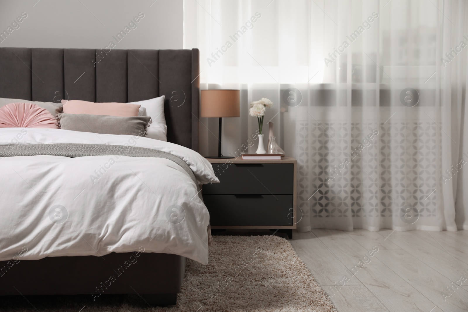 Photo of Comfortable bed with cushions, lamp and different decor on bedside table in room. Stylish interior