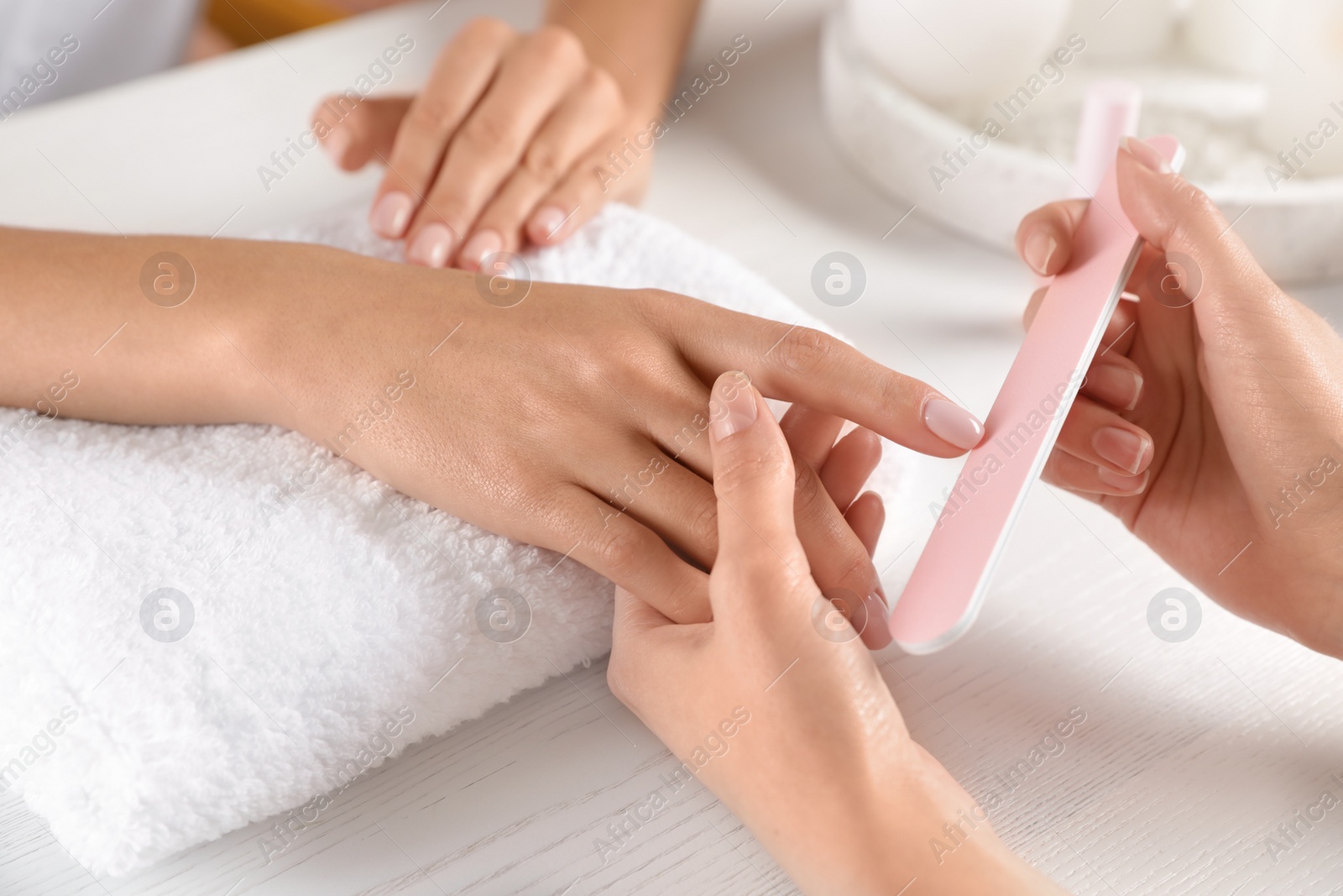 Photo of Manicurist filing client's nails at table, closeup. Spa treatment