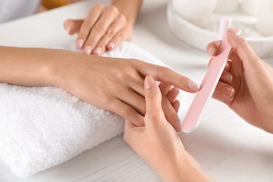 Photo of Manicurist filing client's nails at table, closeup. Spa treatment