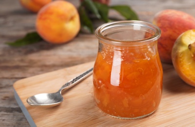 Photo of Jar with tasty peach jam on wooden table