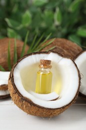 Photo of Bottle of organic coconut cooking oil, leaf and fresh fruits on white table, closeup