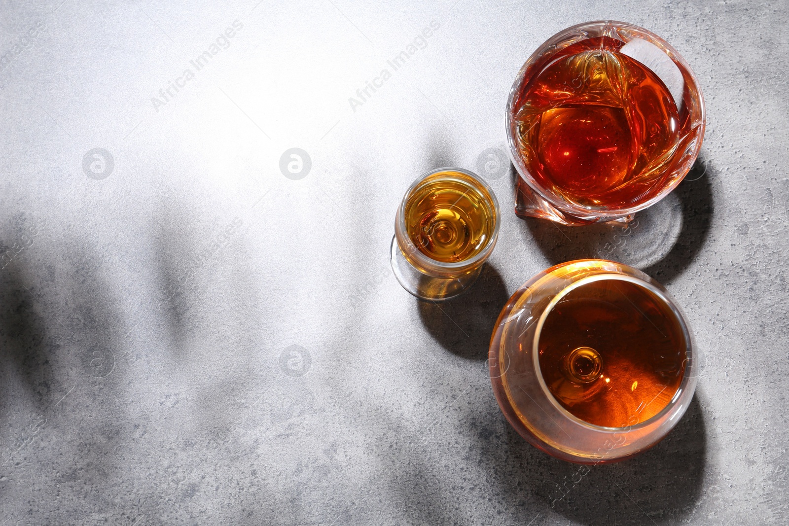 Photo of Different delicious liqueurs in glasses on grey table, flat lay. Space for text