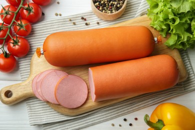 Photo of Board with tasty boiled sausages and products on white wooden table, flat lay