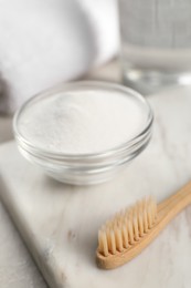 Bamboo toothbrush and glass bowl of baking soda on marble board, closeup