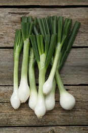 Whole green spring onions on wooden table, flat lay