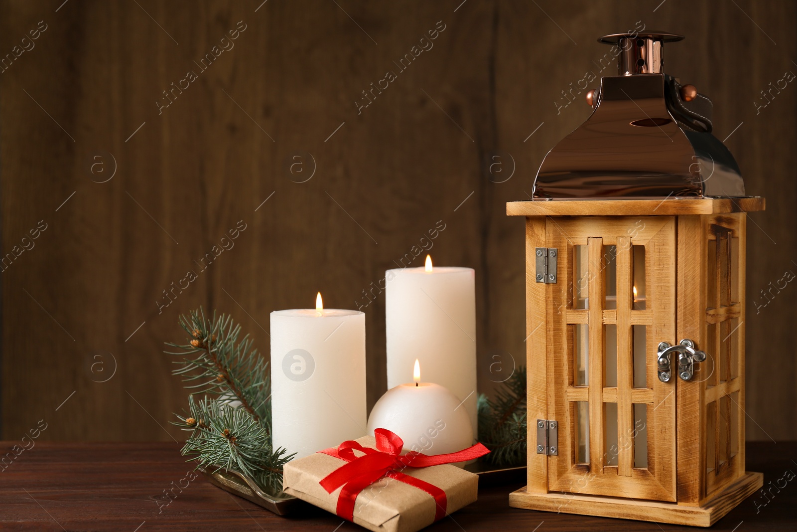 Photo of Composition with burning candles, fir branches and lantern on wooden table, space for text