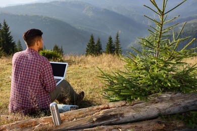 Photo of Man working on laptop outdoors surrounded by beautiful nature, back view