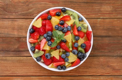 Photo of Delicious fresh fruit salad in bowl on wooden table, top view