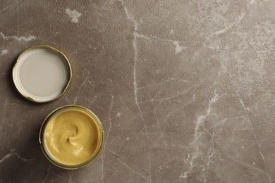 Spicy mustard in glass jar on brown marble table, top view. Space for text