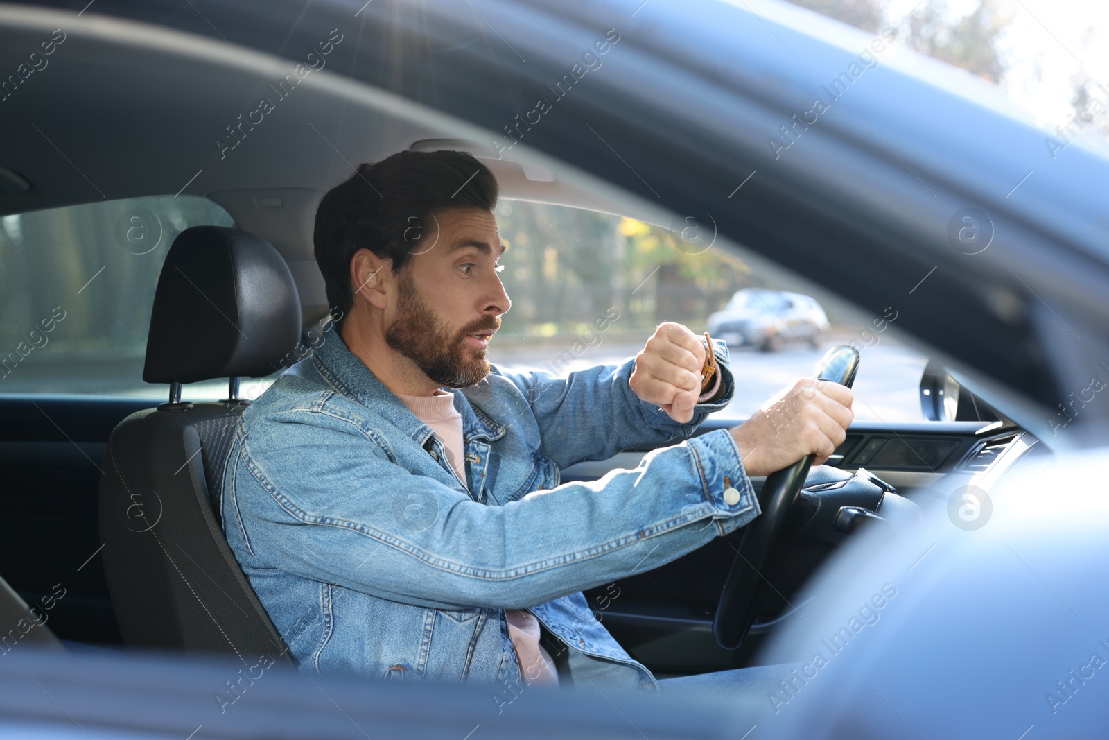 Photo of Emotional man checking time on watch in car. Being late concept