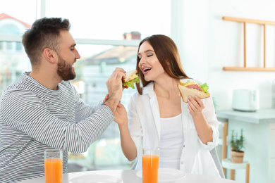 Happy couple having breakfast with sandwiches at table in kitchen